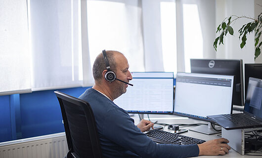 Man sitting at a PC in an office wearing a headset