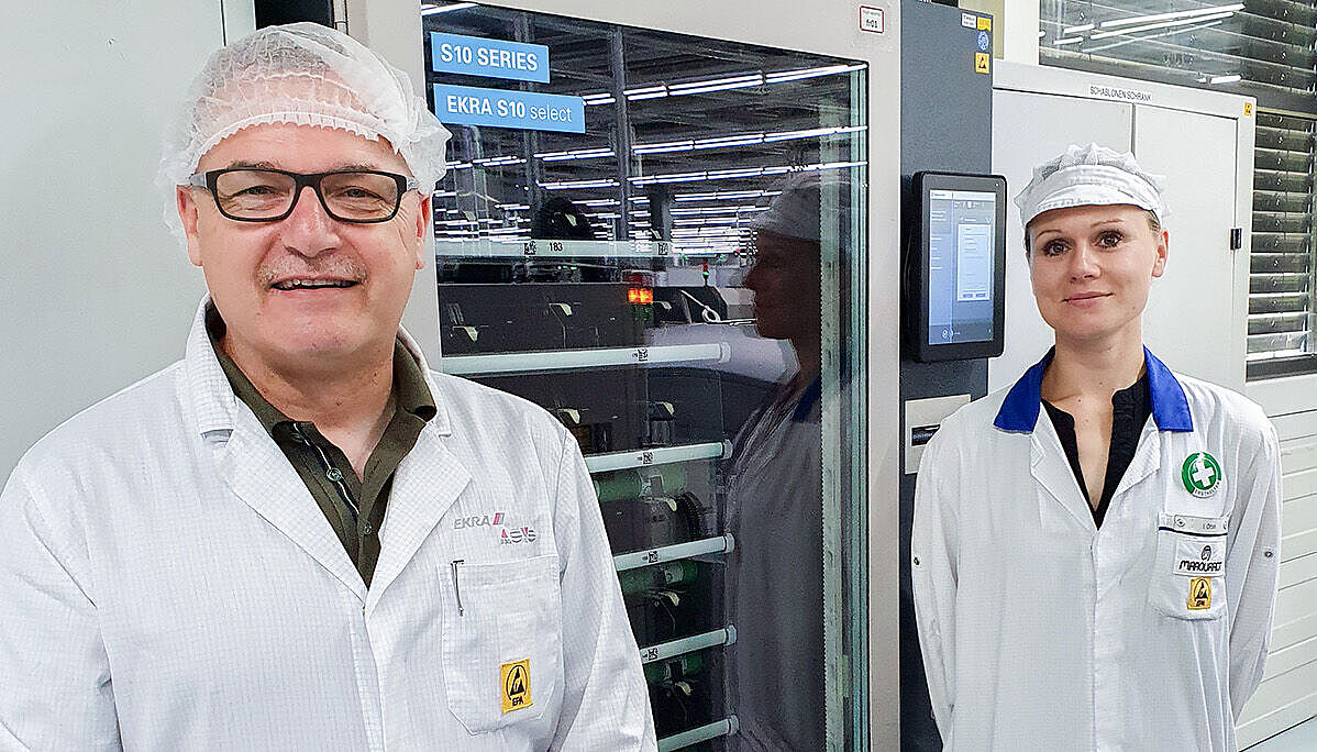 A man and a woman stand to the left and right of a machine and smile at the camera.