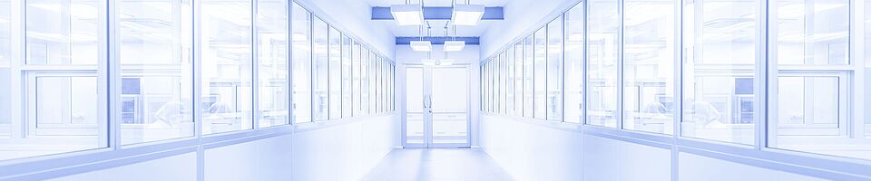 Bright white corridor with a glass door at the end. Windows on both sides reveal visible people behind them. The environment appears sterile.
