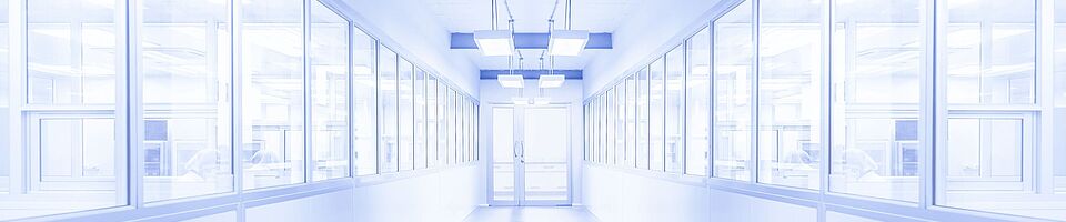Bright white corridor with a glass door at the end. Windows on both sides reveal visible people behind them. The environment appears sterile.