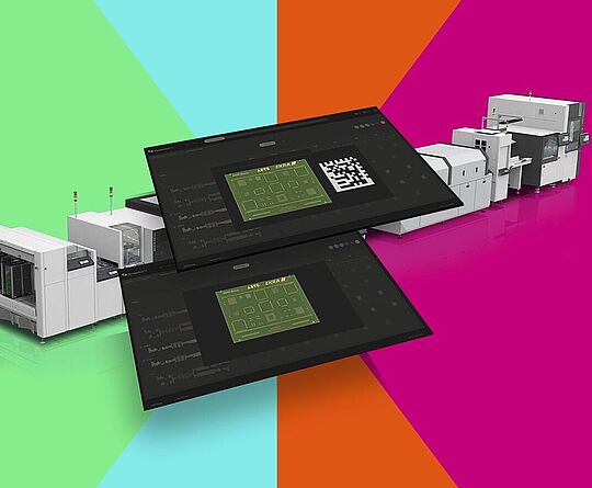 Two screens with a circuit board in the center; a line of machines in the background.