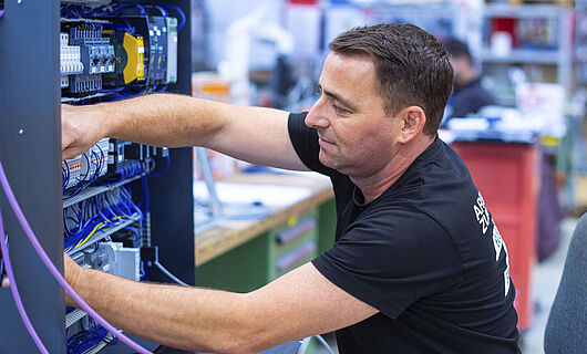 A man in a black T-shirt is sitting and working on a switch box.