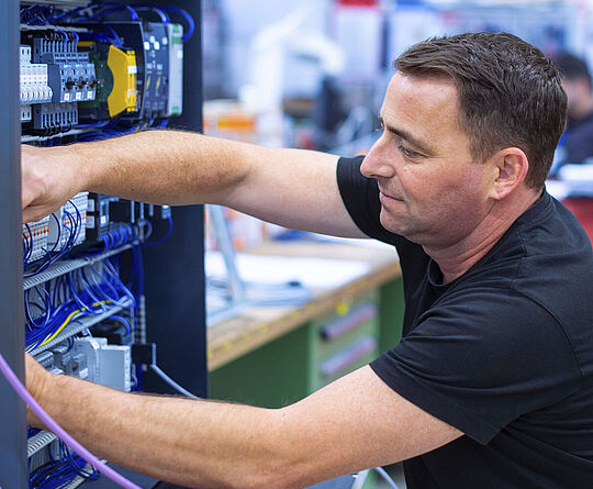 A man in a black T-shirt is sitting and working on a switch box.