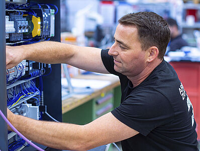 A man in a black T-shirt is sitting and working on a switch box.