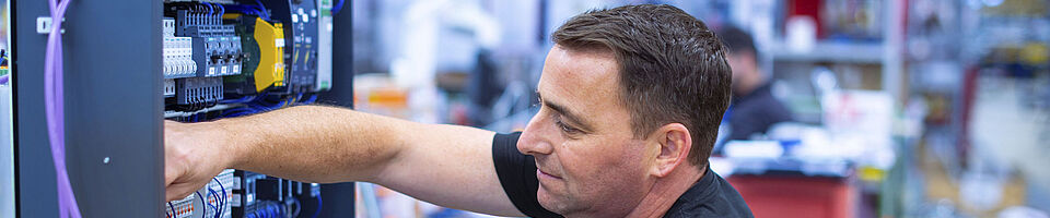 A man in a black T-shirt is sitting and working on a switch box.