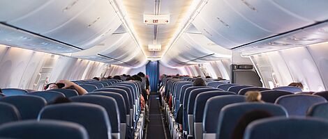 Interior of an airplane in the passenger area, well-lit. The view shows the seat backs arranged in uniform rows.