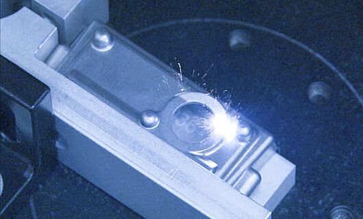Innenansicht einer Laser Maschine, Laser trifft auf silbernes Objekt.