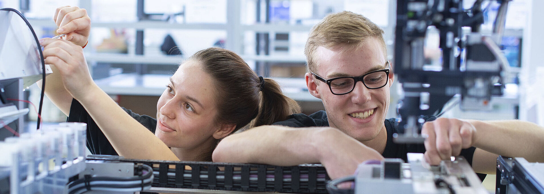 Two young people working together on the inner components of a machine.