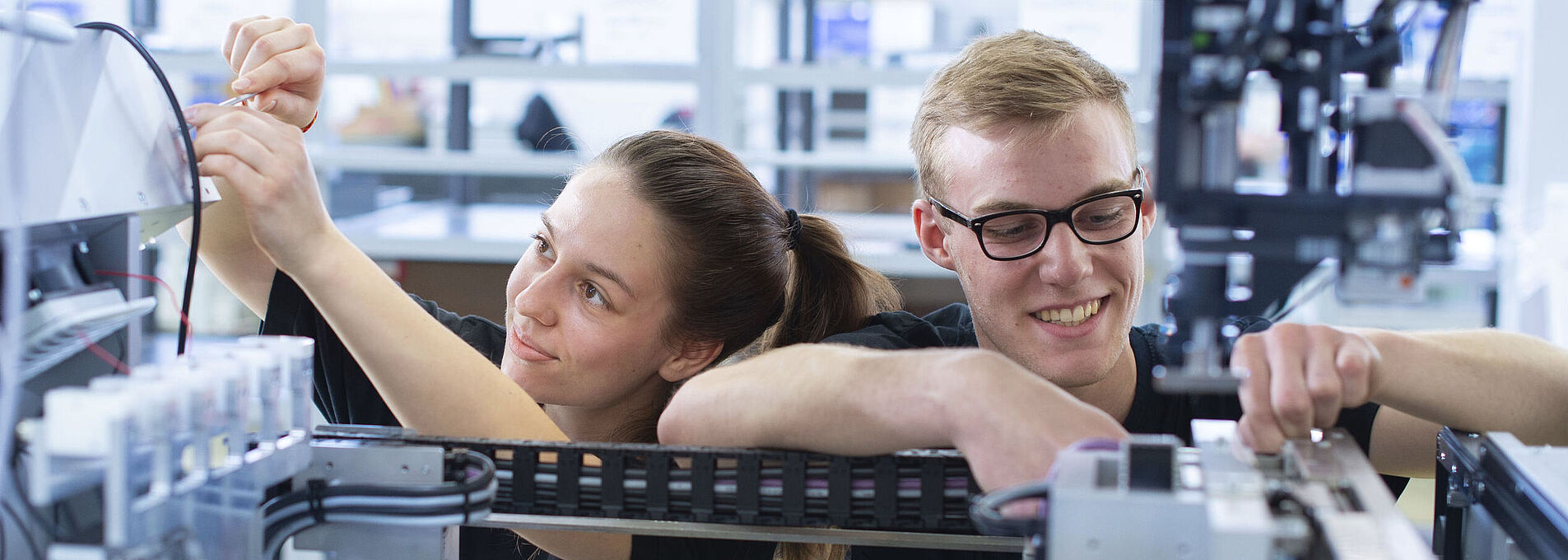 Zwei junge Personen arbeiten gemeinsam am Innenleben einer Maschine.