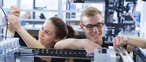 Two young people working together on the inner components of a machine.