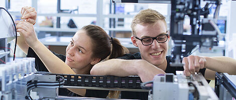 Zwei junge Personen arbeiten gemeinsam am Innenleben einer Maschine.