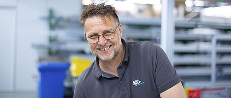 A man is standing in a production hall, smiling.