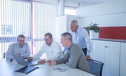 Four men looking together at a laptop in a meeting room
