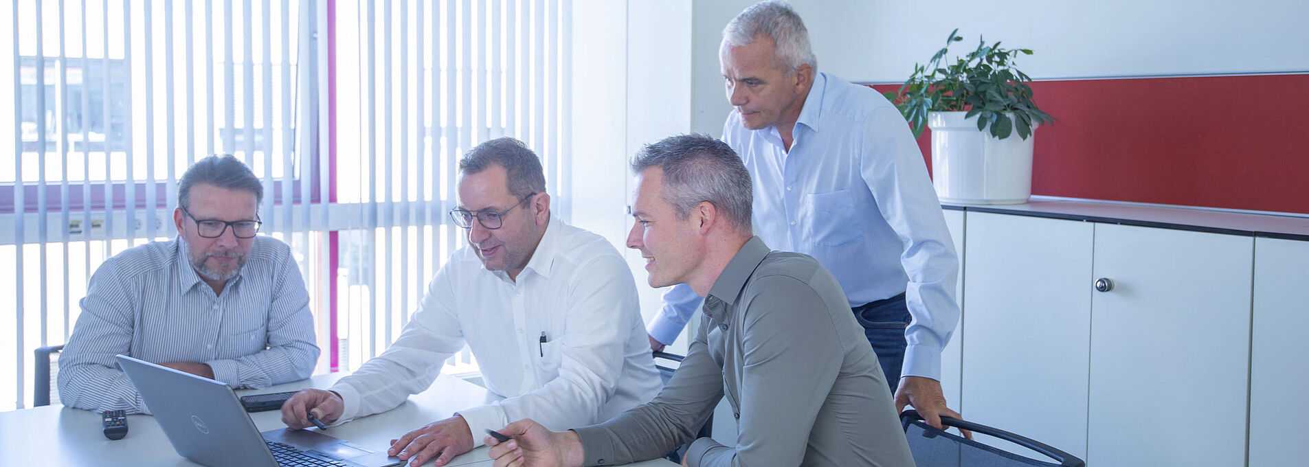 Four men looking together at a laptop in a meeting room