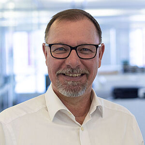 Lächelnder Mann in weißem Hemd in einem hellen Büro.