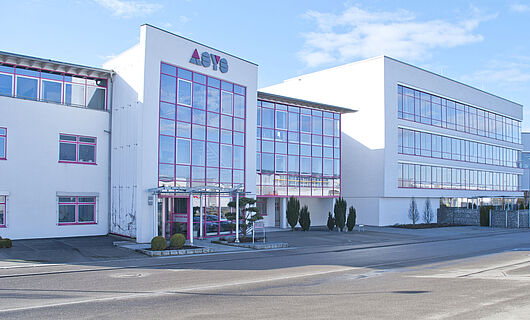 Wide view of a modern ASYS Group company building with a glass façade.