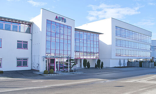 Wide view of a modern ASYS Group company building with a glass façade.