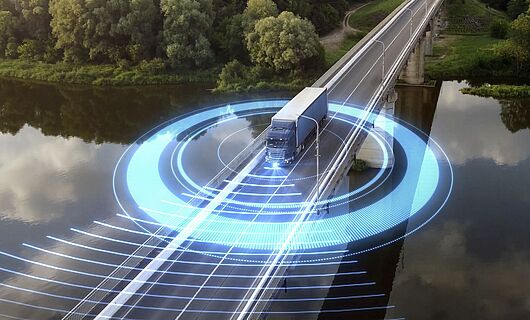 A truck drives across a bridge spanning a river. In the background, a dense forest stretches out. Blue, futuristic glowing lights circle around the truck.