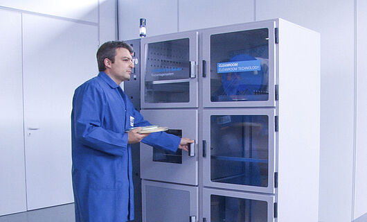 A man wearing a blue overall is standing in front of a machine.