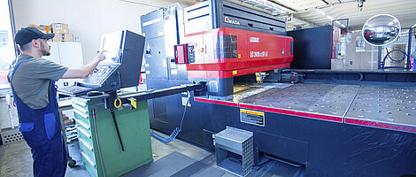 Man working on a laser cutting machine and making adjustments on the control panel.