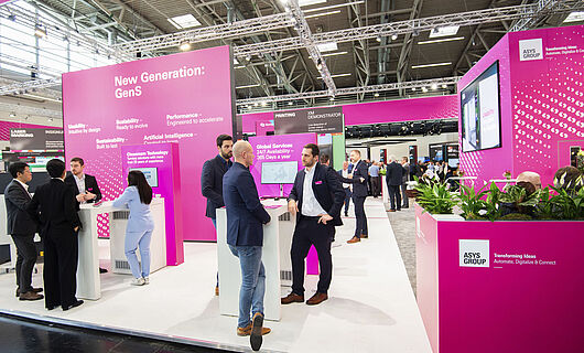 Several men and one woman in suits at a magenta-colored exhibition stand. Standing at bar tables and chatting.