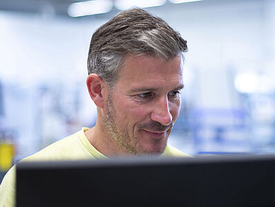 Ein Mann schaut grinsend auf einen Monitor.