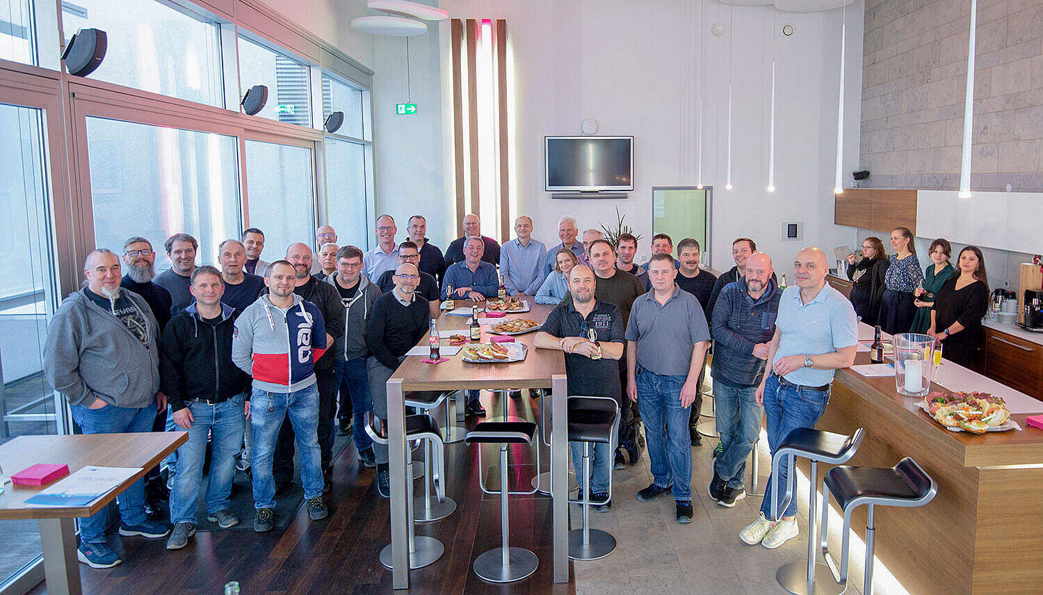 Gruppenbild in einer Lounge hinter und neben einem Stehtisch und einer Bar.