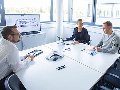 Two men and one woman sitting across from each other at a table in a meeting room.