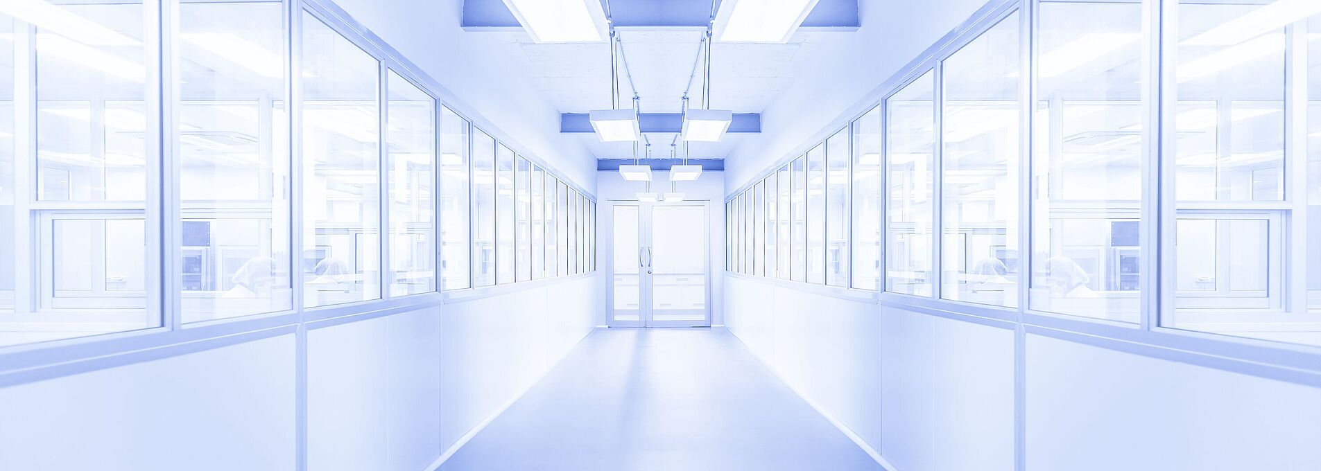 Heller weißer Flur mit einer Glastür am Ende. Links und rechts befinden sich Fenster, hinter denen Personen erkennbar sind. Die Umgebung wirkt steril.
