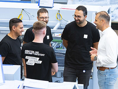 Five men standing in a circle in the middle of a production hall, engaged in discussion.