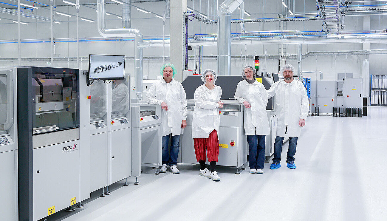 Four people in white lab coats standing in front of and next to machines in a production hall.