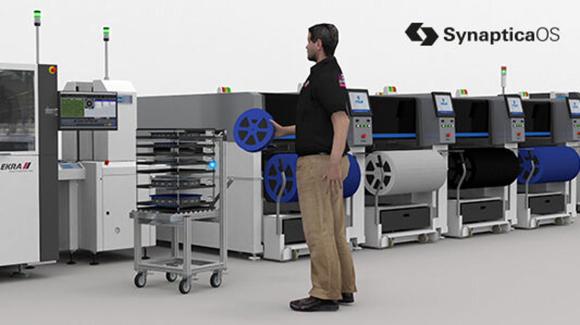A man is holding a component reel in his hand while standing in front of several machines.