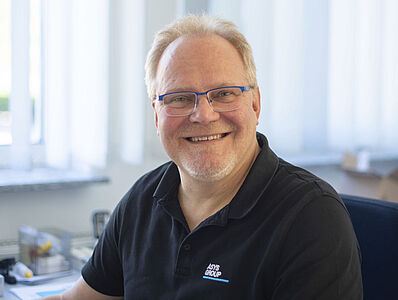 A man is sitting in an office, smiling.