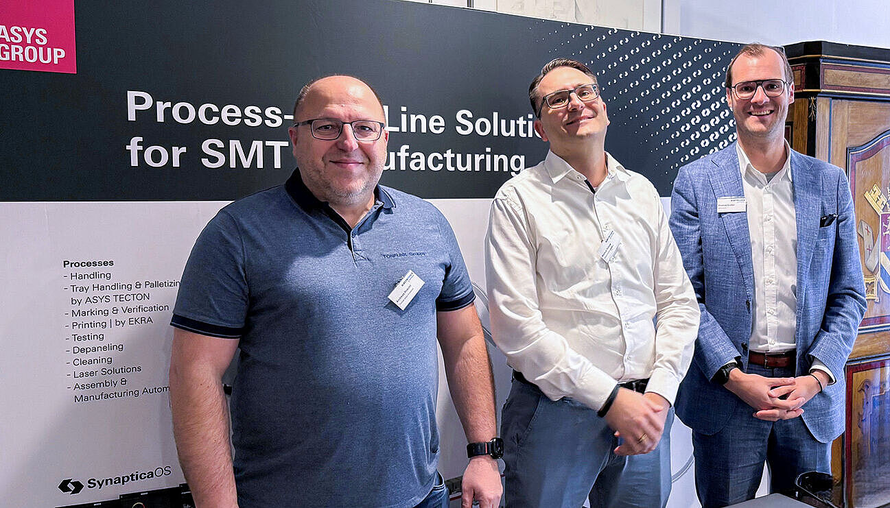 Three smiling men in front of an exhibition booth.
