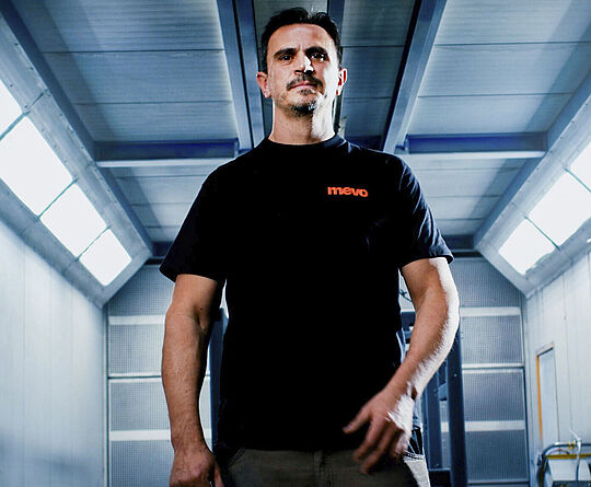 Mann im schwarzen T-Shirt steht in einem Gang mit Beleuchtung von oben.