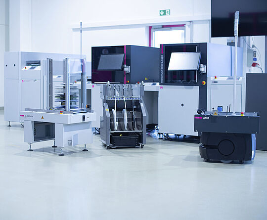 Bauteilrollen-Vorbereitung für Bestückungsautomaten. Ein Feeder-Wagen, M-Station und AMR vor einer SMD-Linie.