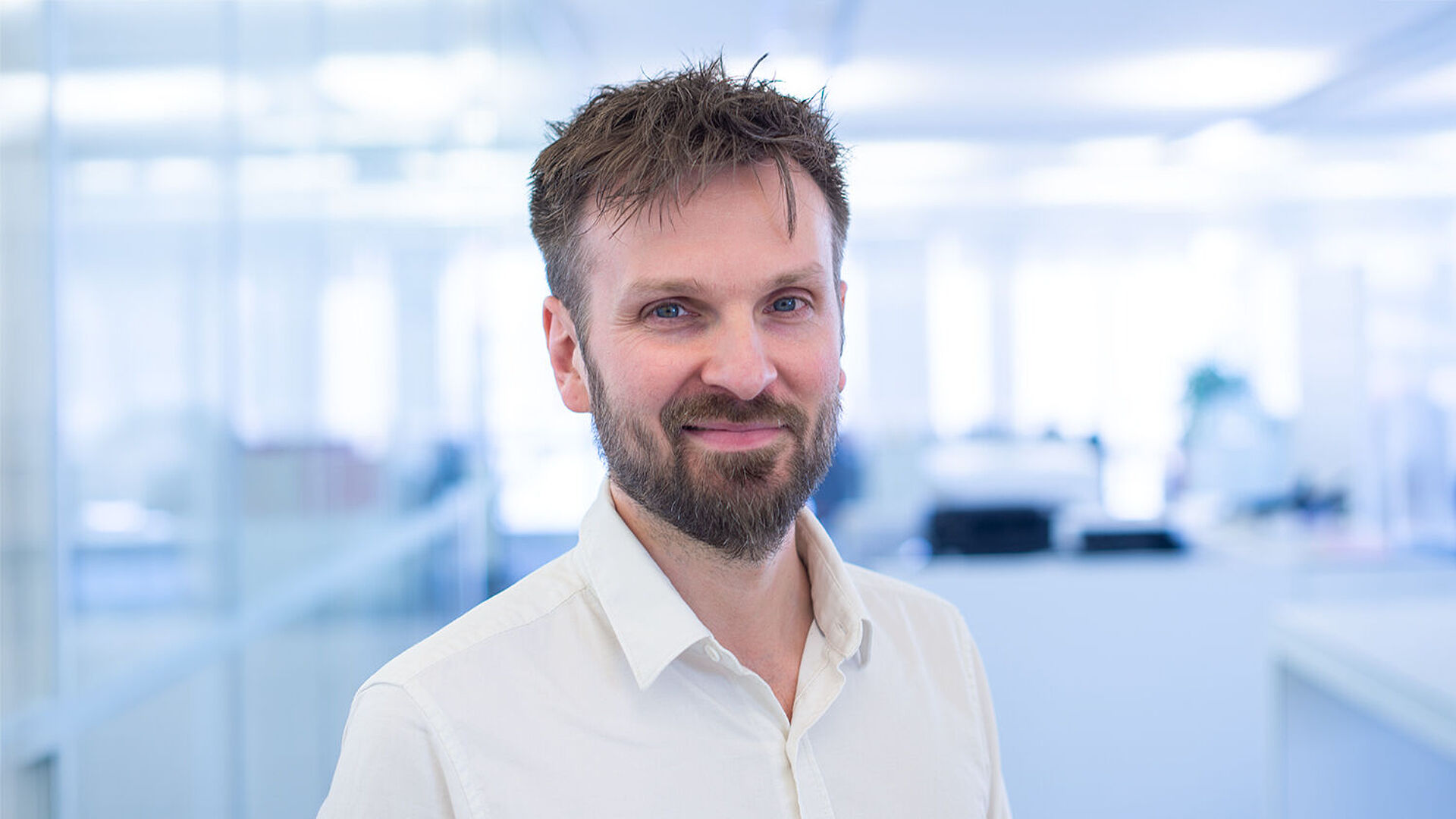 Smiling man in a white shirt in a brightly lit office.