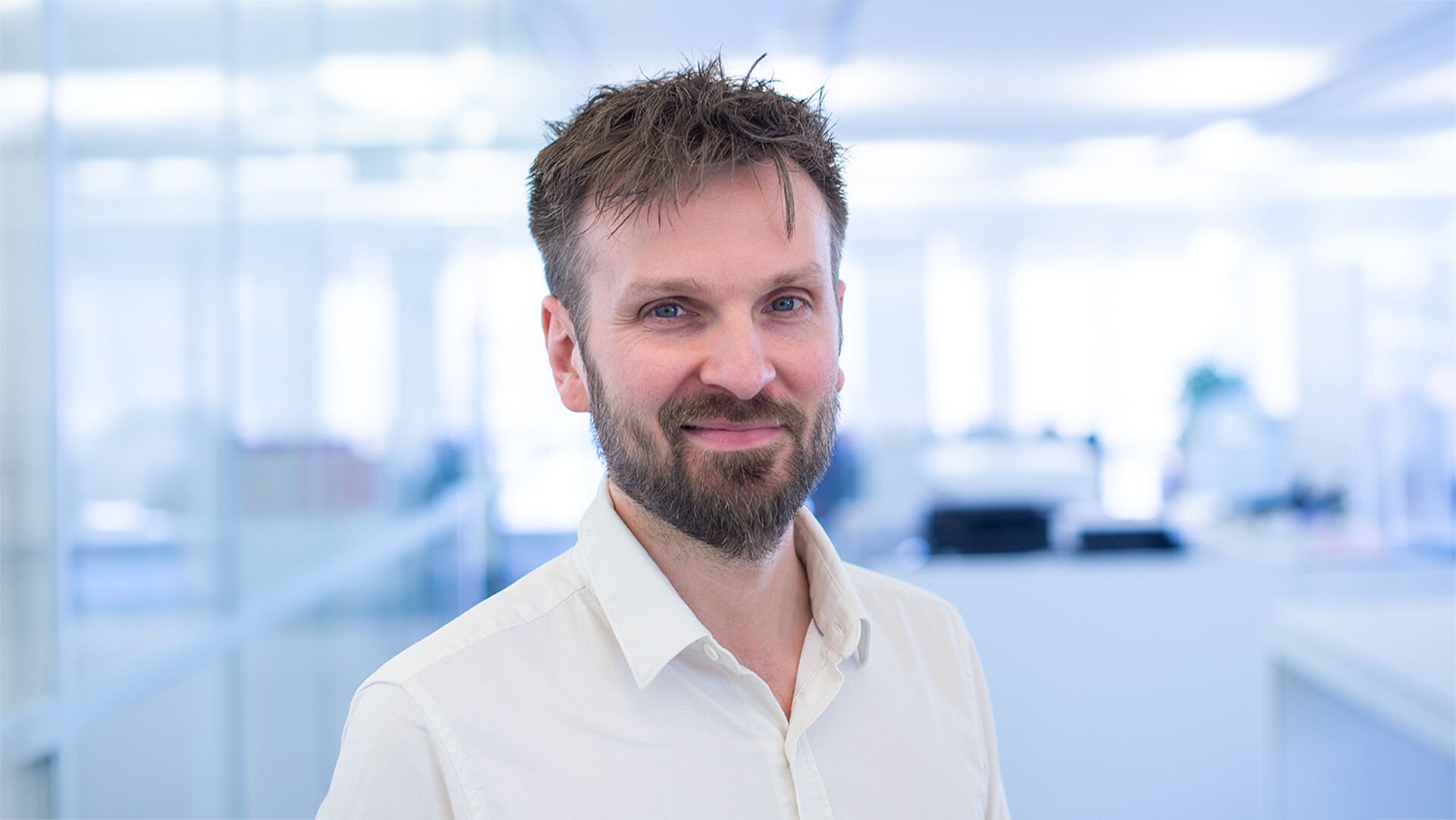 Smiling man in a white shirt in a brightly lit office.