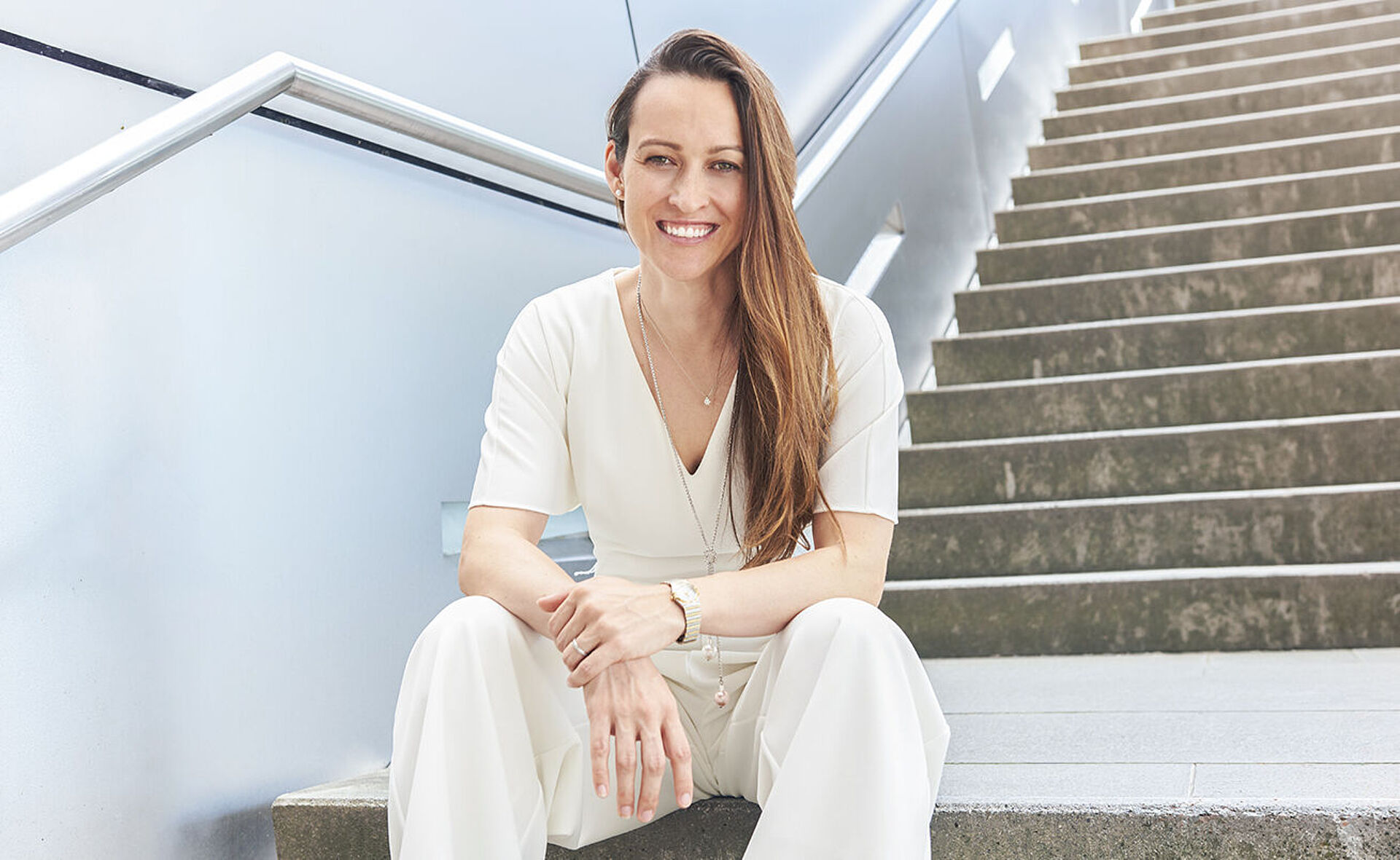 A young woman is sitting on a staircase and smiling.