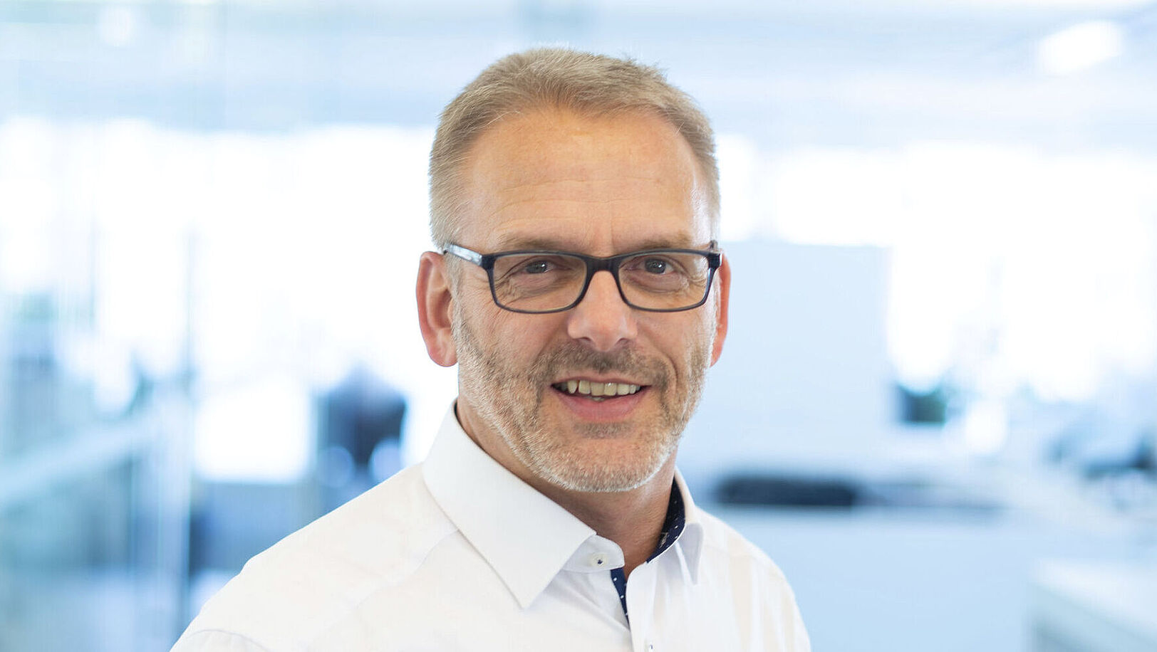 A smiling man is wearing a white shirt.