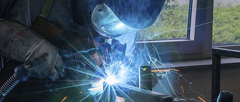 A man is welding a metal structure while wearing protective clothing.