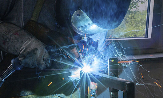 A man is welding a metal structure while wearing protective clothing.