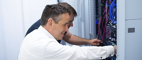 Two men together at an open switch cabinet.