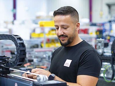 Man in black T-shirt looks at a machine part, spare part in his hand.
