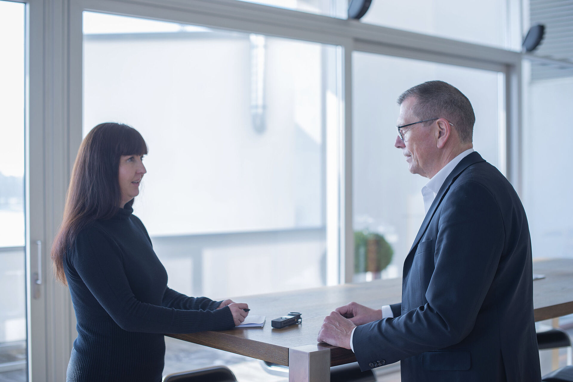 A woman and a man are standing at a bar table and looking at each other.