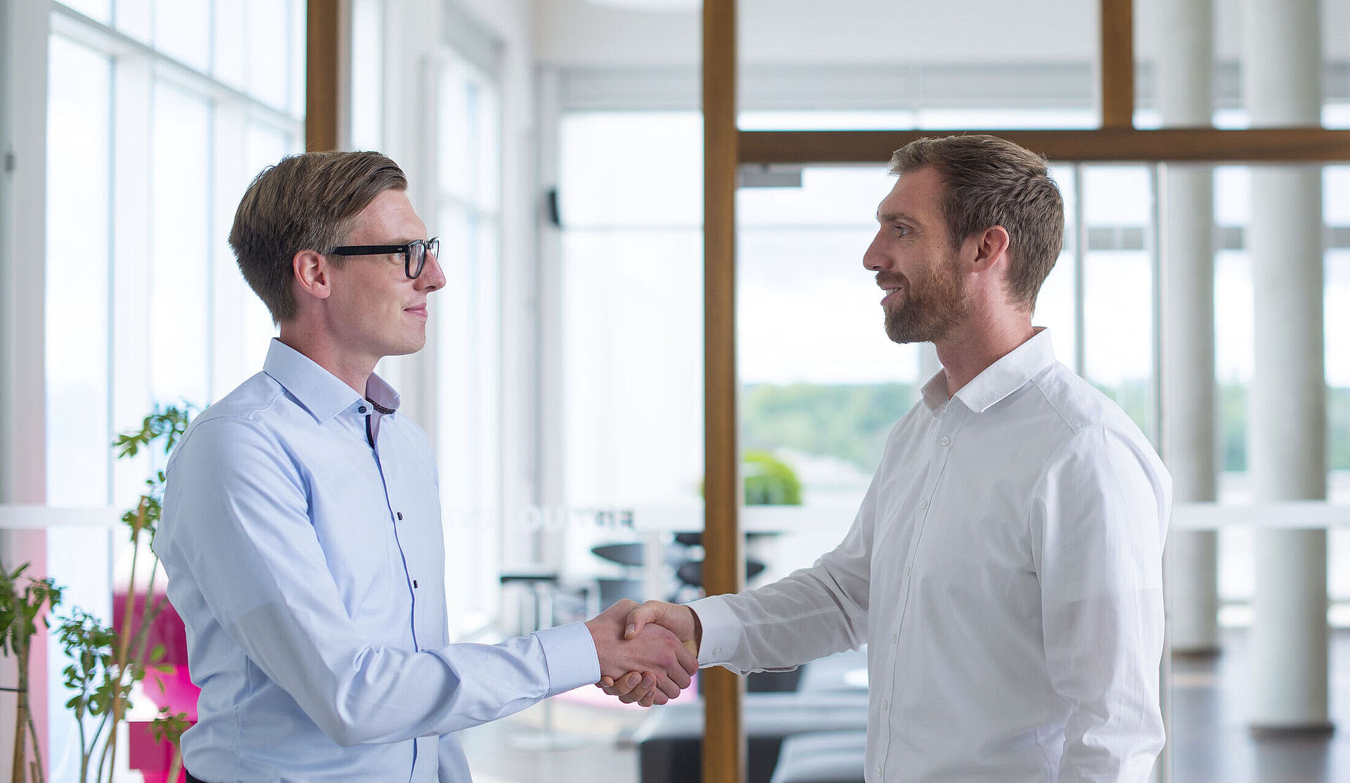 Two men shake hands in a well-lit room.