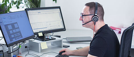Man sitting at a PC in an office wearing a headset