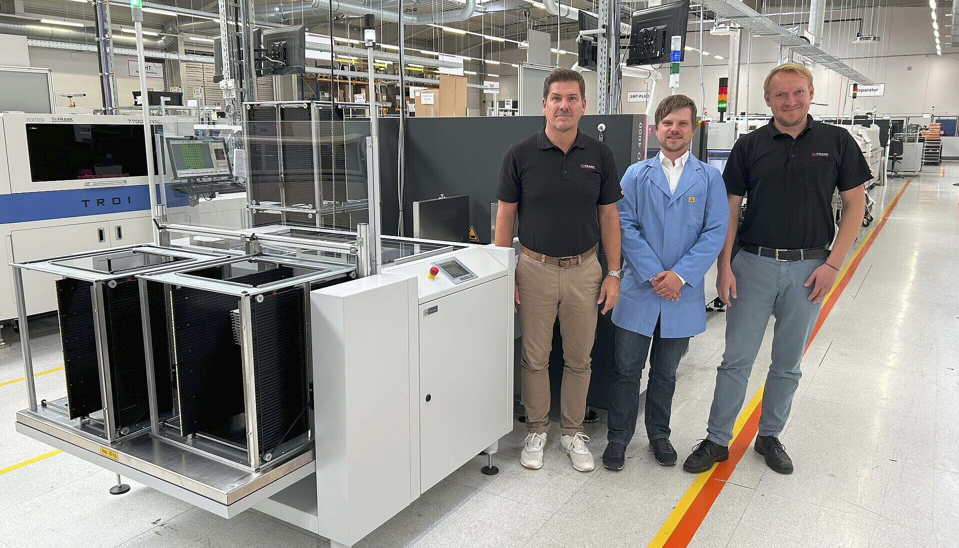 Three men are standing next to a machine in a production hall.