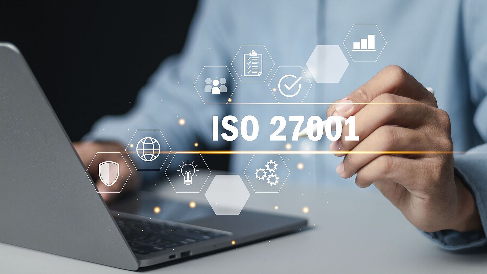 Mann im Hemd sitzt hinter einem Laptop mit einem SmartPen in der Hand. ISO 27001 Schriftzug in der Mitte.