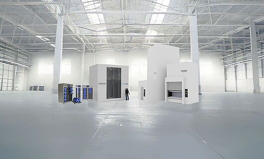 Several machines of different sizes in a huge production hall, with one person standing between them.